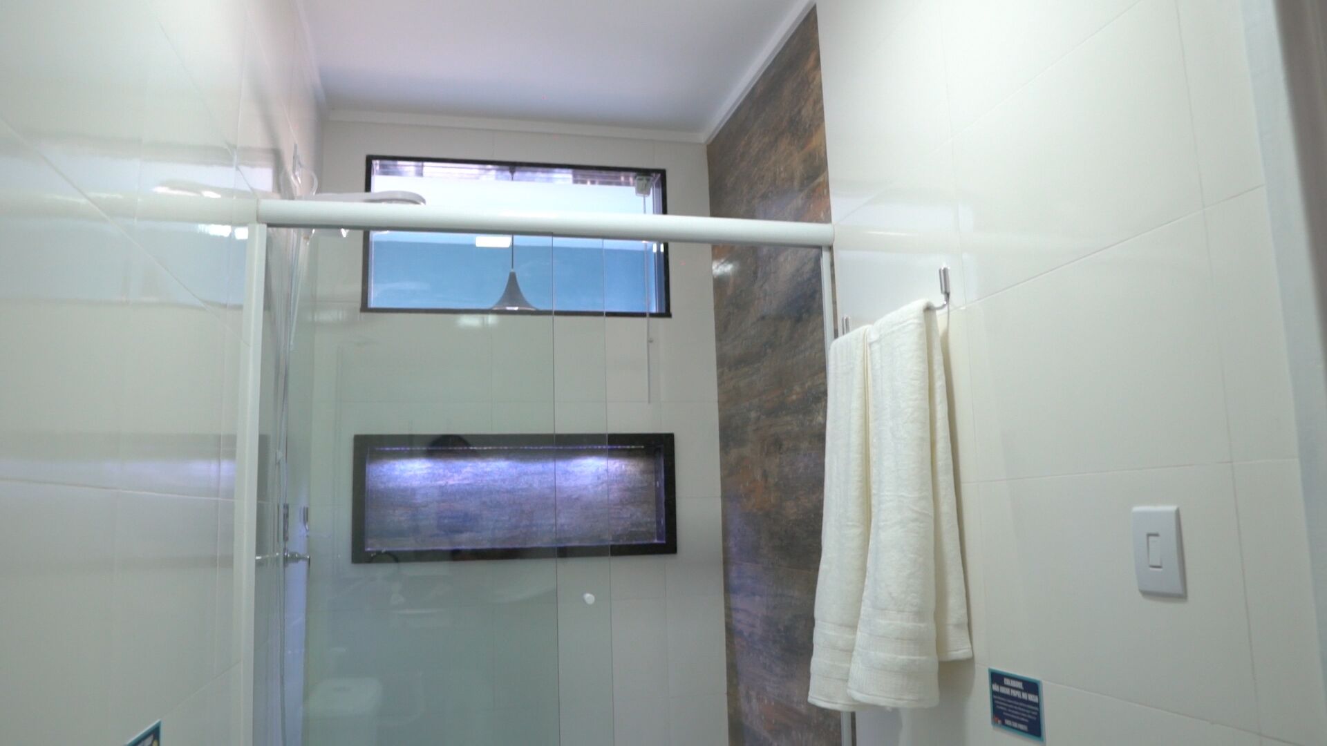 Une salle de bain moderne avec une douche à parois de verre, un porte-serviettes et une vue sur l’extérieur par une fenêtre.