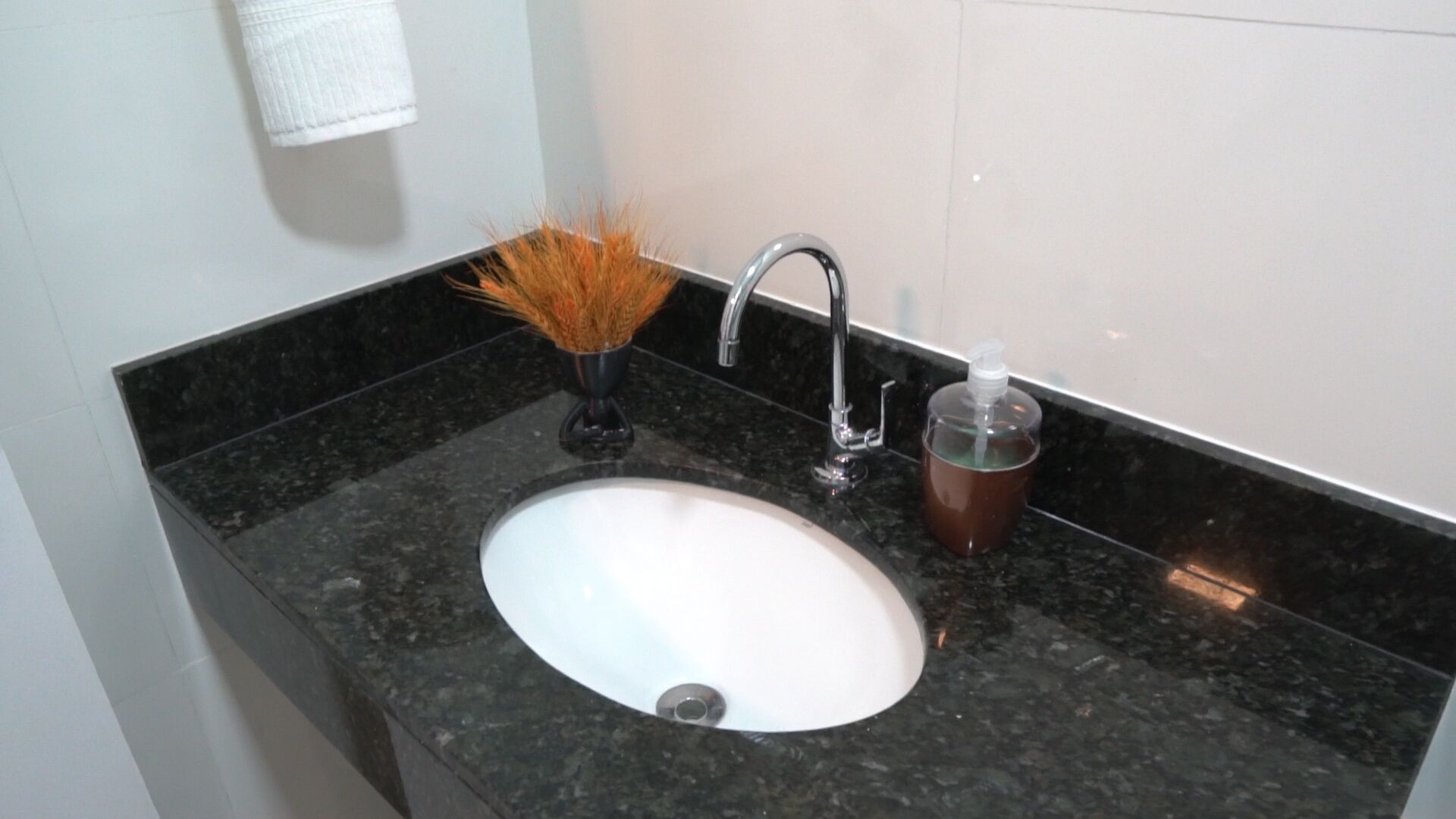 A bathroom sink with a marble countertop, a faucet, a soap dispenser, and a decorative vase with dried plants.