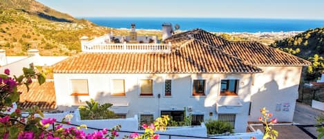 Un edificio blanco con techo de tejas, un balcón y vista al mar.
