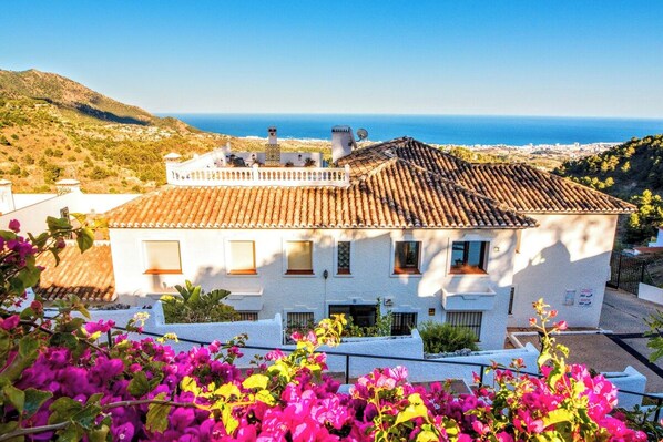 A white building with a tiled roof, a balcony, and a view of the sea.