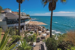 A seaside resort with outdoor seating overlooking the ocean, a building with a balcony, and palm trees. - Beautiful apartment - short walk to the beach (Benalmadena)