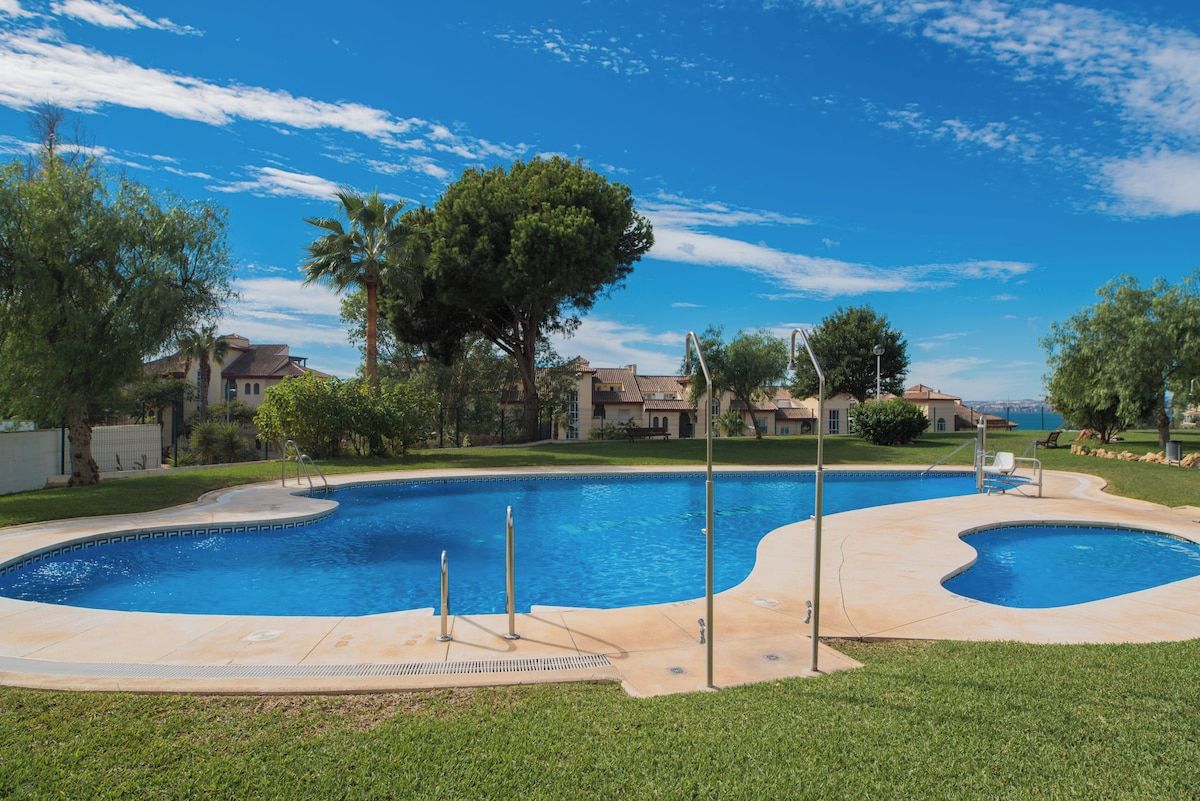 Una piscina con diseño curvo, rodeada de césped y árboles.