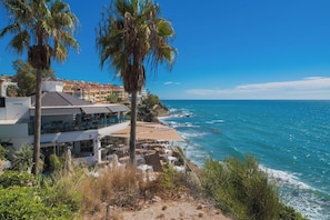 A coastal property with a dining area overlooking the sea, a building with balconies, and a clear sky. - Beautiful apartment - short walk to the beach (Benalmadena)