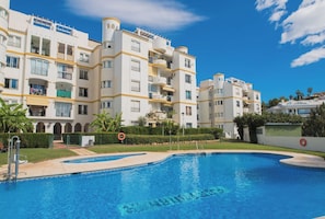 A swimming pool surrounded by a residential building with balconies and a clear sky. - Beautiful apartment - short walk to the beach (Benalmadena)