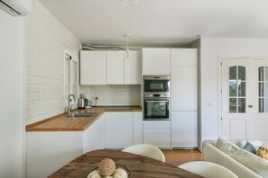 Une cuisine compacte avec des meubles blancs, un plan de travail en bois et un coin repas comprenant une table et des chaises.