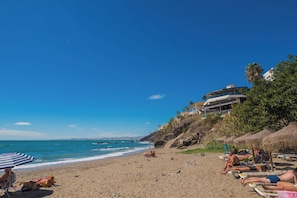 A beach with sun loungers, a clear sky, and a building with a curved roof overlooking the ocean. - Beautiful apartment - short walk to the beach (Benalmadena)
