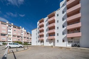 Kerrostalo, jossa on useita kerroksia, parvekkeita, pysäköintialue ja moottoripyörä pysäköitynä sen ulkopuolelle.