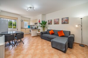A living area with a sofa, chairs, a dining table, and a kitchen in the background.
