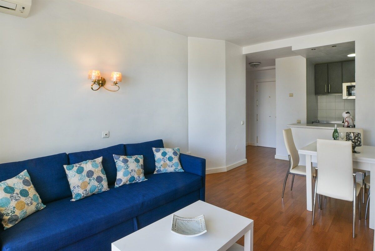 Ein modernes Wohnzimmer mit einem blauen Sofa, einem weißen Couchtisch und einem Essbereich mit Tisch und Stühlen.