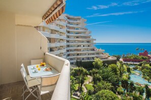 A balcony with a table set for breakfast, overlooking a pool and a building with multiple balconies.