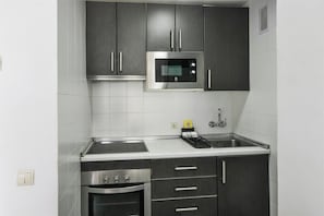 A kitchen with dark cabinets, a stainless steel microwave, a sink, and a stove.