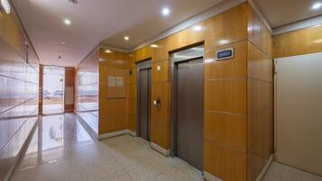 A hallway with wooden paneling, two elevators, and a tiled floor.