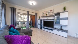 Un salon moderne avec un canapé, un téléviseur et une porte vitrée donnant sur un balcon.