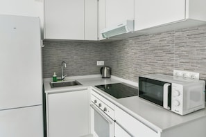 A modern kitchen with white cabinetry, a built-in microwave, a kettle, and a stainless steel sink.