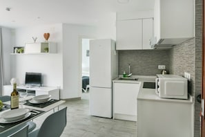 A modern kitchen with white appliances, a dining area with a table set for two, and a TV on a white cabinet. - Torremolinos. Comfortable Apartment. Pool (Torremolinos)