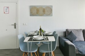 Un coin repas avec une table dressée pour quatre personnes, une bouteille de vin et un tableau accroché au mur.