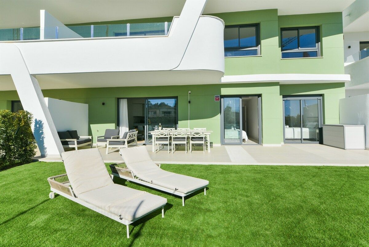 A modern two-story building with a flat roof, a covered outdoor seating area, and a well-maintained lawn.