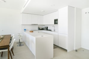 A modern kitchen with white cabinetry, a central island, and a dining area with a wooden table and white chairs. - Premium apartment with luxury spa, garden & pool (La Cala de Mijas)