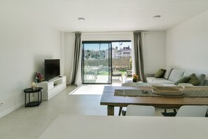 A modern living room with a flat-screen TV, a dining table, and a sofa with cushions. - Premium apartment with luxury spa, garden & pool (La Cala de Mijas)