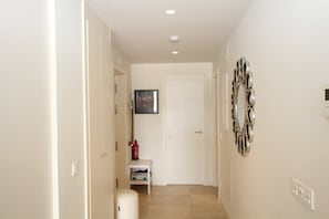 A hallway with a white door, a small table with a vase, and a wall-mounted mirror.