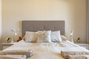 A neatly made bed with a grey headboard, two bedside lamps, and a small vase with flowers on each side.