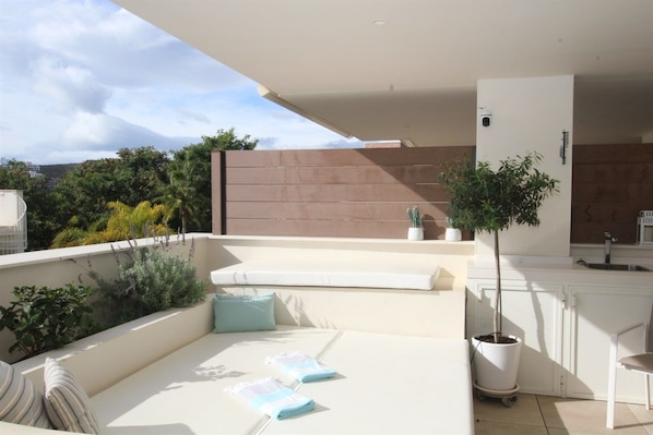 A modern outdoor living area with a sofa, cushions, a small table, and a potted plant.