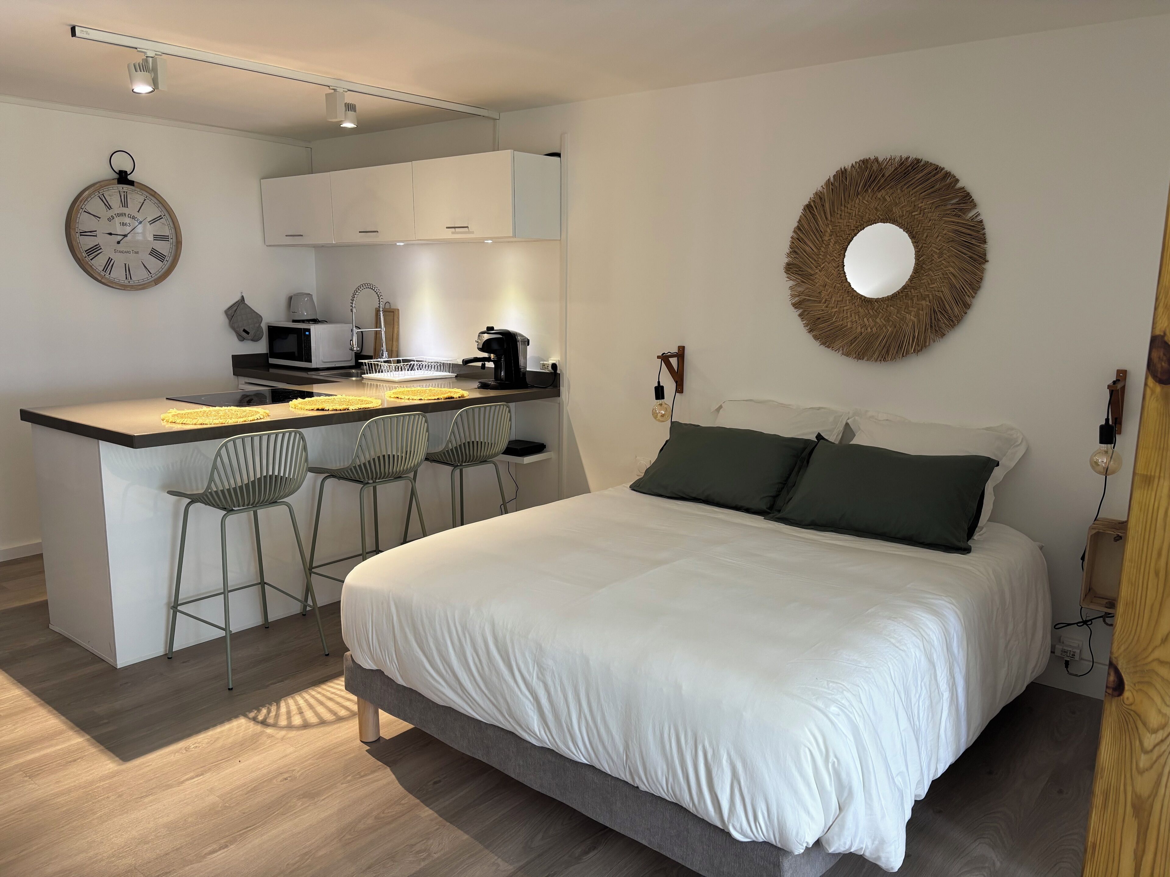 A modern bedroom with a large bed, a small kitchenette, and a dining area.
