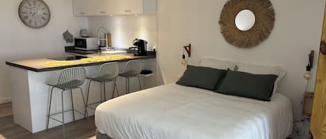 A modern bedroom with a large bed, a small kitchenette, and a dining area.