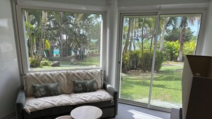 A modern living room with a sofa, two round tables, and a view of a lush garden through large windows. - Spacious studio on the seafront, newly renovated (Le Gosier)