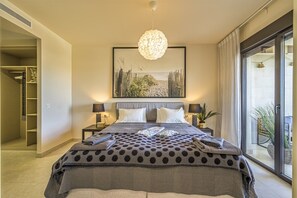 Ein Schlafzimmer mit einem großen Bett, Blick ins Freie durch eine Schiebetür und einem Gemälde an der Wand.