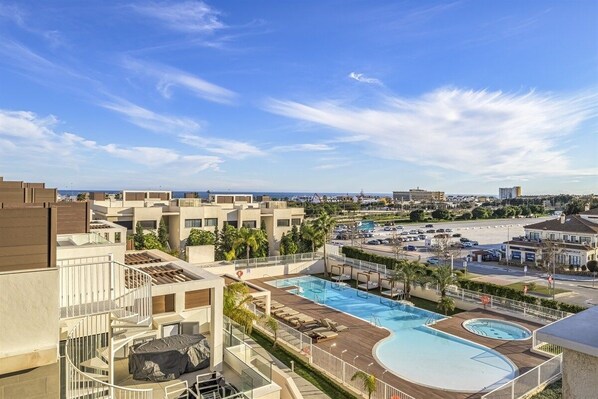 A rooftop swimming pool with lounge chairs, surrounded by buildings and a clear sky.