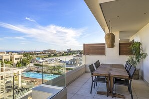 Ein Balkon mit Esstisch und Stühlen, mit Blick auf ein Schwimmbad und eine Stadtlandschaft.