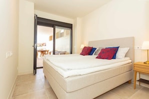 A bedroom with a bed, a nightstand, and a view through a glass door to a dining area.