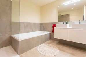 A modern bathroom with a bathtub, a round rug, and a large mirror above the sink.