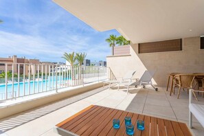 A balcony with a pool, lounge chairs, a table with glasses, and a view of the city.
