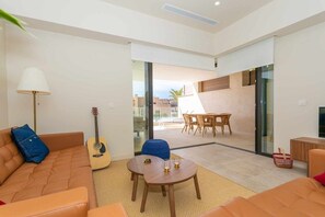 A modern living room with a sofa, a coffee table, and a guitar. There is a dining area with a table and chairs. - Walk to Beach! Premium apartment pool & gym (La Cala de Mijas)