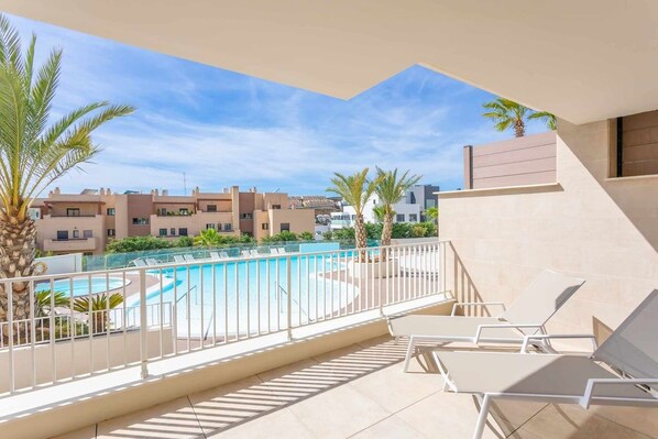 A balcony with a pool, lounge chairs, and a view of other buildings.