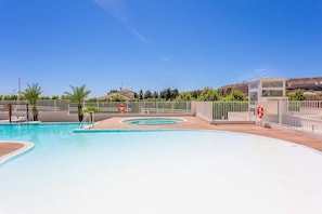 A swimming pool with a wooden deck, surrounded by a white fence and palm trees. - Modern 3 bedroom apartment, very close to beach (La Cala de Mijas)