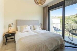 Een slaapkamer met een groot bed, een nachtkastje, een lamp en uitzicht op de natuur via een glazen schuifdeur.