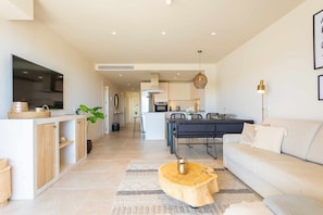 A modern living room with a sofa, a coffee table, and a TV. There is a kitchen area in the background with cabinets and a dining table. - Amazing seaview near the beach! (La Cala de Mijas)