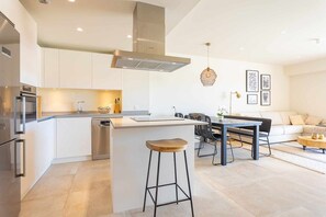 Eine moderne Küche mit Kochinsel, Edelstahlgeräten und einem Essbereich mit schwarzem Metalltisch und Stühlen.