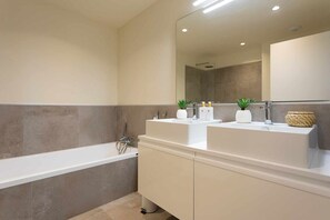 Een moderne badkamer met een badkuip, twee wastafels en een grote spiegel.