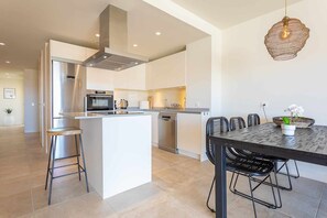 A modern kitchen with a central island, stainless steel appliances, and a dining area with a dark table and black chairs. - Amazing seaview near the beach! (La Cala de Mijas)