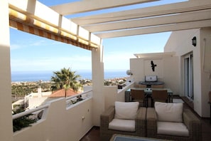 A balcony with wicker furniture, a small table, and a view of the sea. - Spacious, bright penthouse 3 terraces & sea view (Calahonda)