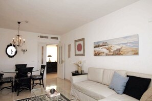 A living room with a white sofa, a glass coffee table, a chandelier, and a painting on the wall. - Spacious, bright penthouse 3 terraces & sea view (Calahonda)