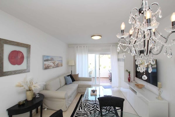 A modern living room with a chandelier, a sofa, a glass coffee table, and a television.