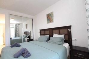 A hotel room with a large bed, a bedside table, a nightstand, a mirror, and a painting on the wall.