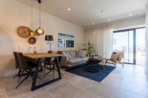 A modern living room with a dining area, a sofa, a coffee table, and a large window.