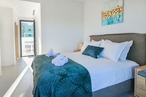 A modern bedroom with a large bed, a painting on the wall, and a view of the outside.