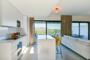 A modern kitchen with a central island, a dining area with yellow chairs, and large windows offering a view of the landscape.